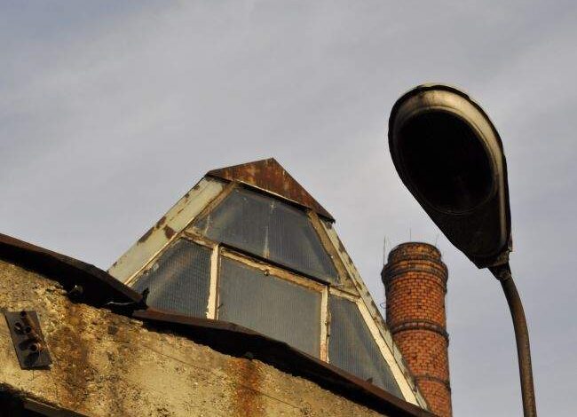 Burzowa rura na dachu z widokiem na stary komin przemysłowy, zdjęcie architektury i przemysłowej konstrukcji, z pochmurnym niebem w tle, idealne do projektu modernizacji obiektów przemysłowych.