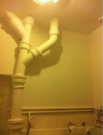 Rury kanalizacyjne i instalacje w łazience, widok na system rur z PVC. Przedstawia instalację sanitarną w budynku, użyteczne dla usług naprawczych i konserwacyjnych.