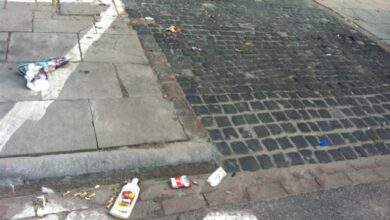 Brudna ulica z śmieciami na chodniku i jezdni, drobne odpadki, brak czystości, nieestetyczna przestrzeń miejską, zanieczyszczone otoczenie, problem porządkowania przestrzeni publicznej, brak dbałości o estetykę miasta.