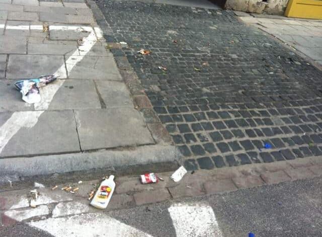 Brudna ulica z śmieciami na chodniku i jezdni, drobne odpadki, brak czystości, nieestetyczna przestrzeń miejską, zanieczyszczone otoczenie, problem porządkowania przestrzeni publicznej, brak dbałości o estetykę miasta.