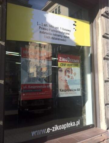 Widok zewnętrzny apteki z plakatami informacyjnymi i reklamowymi, w tym dla apteki internetowej e-zikoapteka.pl, w centrum miasta, z widoczną ulicą Kasprowicza 68.