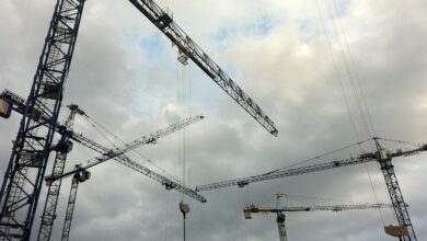 Konstrukcja dźwigów budowlanych na placu budowy, pod chmurami, podkreślają proces wznoszenia obiektów, kluczowe dla branży budowlanej i inwestycyjnej.