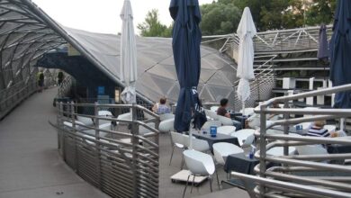 Nowe otwarte patio z parasolami i stolikami w nowoczesnej przestrzeni gastronomicznej na zewnątrz z widokiem na zieleniec i wzniesione mostki, idealne na relaks i spotkania.