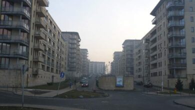 Nowe osiedle mieszkaniowe w mieście, budynki wielopiętrowe z balkonami i ulicą w centrum, panorama nowoczesnej architektury, codzienne życie mieszkańców, komfort i funkcjonalność.