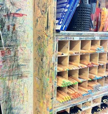 Kolorowe kredki i zarysowane kreski na wypisanej ścianie, pełne artykułów piśmienniczych i kredek do rysowania, idealne do kreatywnej pracy i nauki dla dzieci i dorosłych.