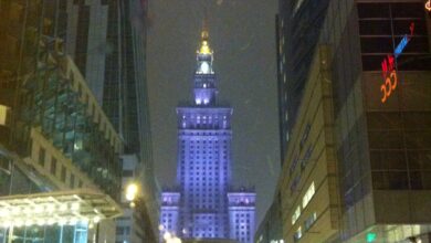 Wieża w Warszawie nocą, oświetlona sztucznym światłem, z nowoczesnymi budynkami wokół, zimowa sceneria z opadami śniegu, idealna na zdjęcia i eksplorację miasta.