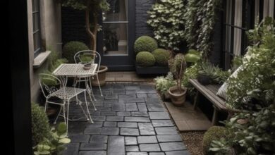 Czarna brukowa ścieżka w ogrodzie z zielonymi roślinami i meblami z metalu, nowoczesny ogród na patio w stylu skandynawskim, outdoorowe miejsce wypoczynkowe, aranżacja małej przestrzeni, elegancki ogród w centrum miasta.