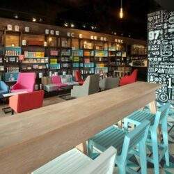 Kolorowe, nowoczesne wnętrze kawiarni lub restauracji z wygodnymi kanapami i stolikami, regulaminem wystroju z drewnianych elementów i akcentami graficznymi, idealne do relaksu lub spotkań towarzyskich.