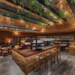 Nowoczesna restauracja z zielonymi roślinami na suficie i ceglanymi ścianami, komfortowe miejsce do spotkań i jedzenia, idealne na imprezy i biesiady.