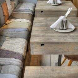 Nowoczesne wyposażenie restauracji, stoliki z drewnianym wykończeniem, eleganckie nakrycia stołowe z solniczkami i pieprzniczkami, przytulna atmosfera, idealne miejsce na spotkania biznesowe i rodzinne.