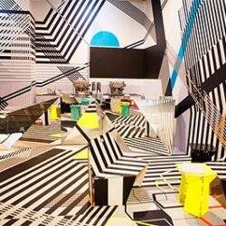 Nowoczesne biuro z abstrakcyjnym wzorem na ścianach i meblami w stylu minimalistycznym, idealne do kreatywnych przestrzeni biurowych.