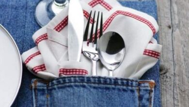 Wygląd zastawy stołowej w kieszeni jeansowej na drewnianym stole, idealne na eleganckie przyjęcie, z talerzem, sztućcami i szklanką z lemoniadą, dostosowane do stylu Optima.