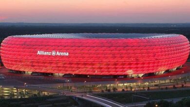 Stadion Allianz Arena oświetlony na czerwono, nowoczesna architektura, wieczorny widok, popularne miejsce sportowe i widowiskowe, w tle delikatny zachód słońca.