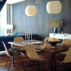 Stylowa jadalnia w nowoczesnym wnętrzu z drewnianym stołem i rattanowymi krzesłami, eleganckie lampy wiszące oraz dekoracje z kwiatami, harmonijne i przytulne aranżacje dla domu.