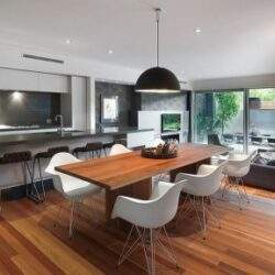 Nowoczesny aneks kuchenny połączony z jadalnią i salonem, wnętrze z eleganckimi meblami, parkietem i dużymi oknami zapewniającymi dostęp do naturalnego światła.