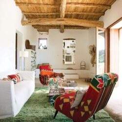 Przytulny salon z drewnianym sufitem, kolorowe fotele i sofa, naturalne światło, wnętrze w stylu rustykalnym, idealne do relaksu i spotkań rodzinnych.