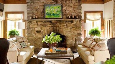 Przytulny salon z kamiennym kominkiem, dwoma sofami i naturalnym światłem, idealny do relaksu i spotkań rodzinnych. Wnętrze z elementami drewnianymi i roślinnymi dekoracjami, tworzące ciepłą atmosferę.