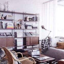 Regał na książki w nowoczesnym, jasnym salonie pełnym naturalnego światła, z elegancką sofą i wygodnym krzesłem, idealne miejsce do pracy i relaksu.