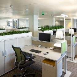 Biuro z nowoczesnym wyposażeniem, stanowisko pracy z komputerem i roślinami na tle otwartego przestrzeni biurowej nowoczesny design, ergonomiczne miejsce do pracy, biurowe meble i roślinność optymalizacja przestrzeni biurowej.