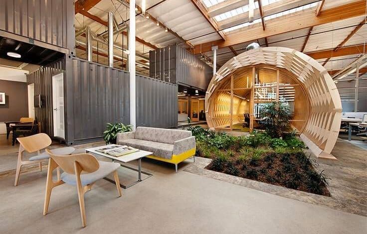 Nowoczesna strefa relaksu w biurze z komfortowym sofa, drewnianymi krzesłami i zielenią w inspirującym wnętrzu. Idealne miejsce do odpoczynku i spotkań branżowych w optymalnym środowisku pracy.