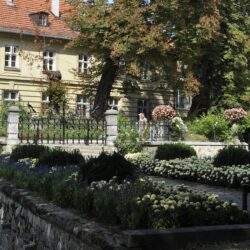 Piękny ogród z kwiatami w pobliżu zabytkowego budynku, idealny do odpoczynku i relaksu na świeżym powietrzu. Arboretum, nasadzenia, alejki i piękna architektura dla miłośników zieleni.