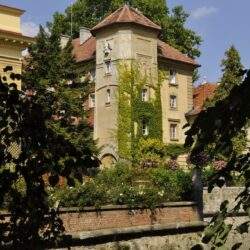 Ekskluzywny budynek z wieżą, otoczony zielenią i kwitnącym ogrodem, idealne miejsce na działalność optima i rozwój biznesu w komfortowej atmosferze.