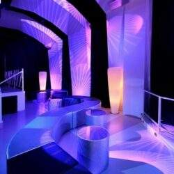 Elegancki, nowoczesny salon z unikalnym oświetleniem w odcieniach fioletu i niebieskiego, idealny do relaksu i spotkań biznesowych, zapewniający komfort i ekskluzywną atmosferę.