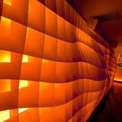 Nowoczesna, podświetlana ściana z geometricznych paneli, elegancka aranżacja wnętrza hotelu lub restauracji, tworząca luksusową atmosferę, inspirujące miejsce na wydarzenia i spotkania biznesowe.