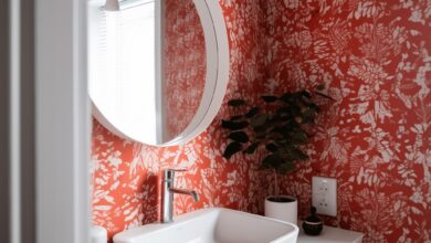 Umywalka w nowoczesnej łazience z czerwono-białą tapetą roślinną, lustro nad umywalką, dekoracyjne dodatki, minimalistyczny design, eleganckie wnętrze, funkcjonalny i estetyczny wystrój, naturalne akcenty, aranżacja łazienki dla domu i biura.