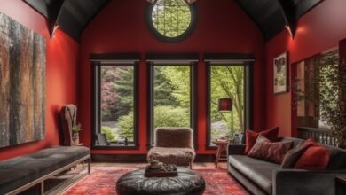 Przytulny pokój z czerwonymi ścianami i dużymi oknami, elegancki wystrój, wygodne meble, dywan i naturalne światło, idealny do relaksu i wypoczynku w domu.