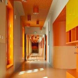 Nowa, kolorowa hala w budynku przedszkola lub żłobka, z dominacją odcieni pomarańczowego i żółtego, z kreatywnym, przyjaznym designem i dekoracjami, idealna do optymalizacji środowiska dla dzieci.