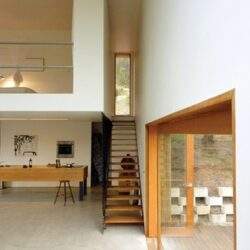 Nowoczesny, minimalistyczny dom z drewnianymi schodami i dużymi przeszkleniami, wnętrza z naturalnym światłem, aranżacja przestrzeni, współczesny design, optymalne rozwiązania funkcjonalne.