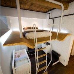 Łóżko na antresoli z drewnianą platformą i drabinką w nowoczesnym wnętrzu, idealne rozwiązanie do optymalizacji przestrzeni mieszkalnej.