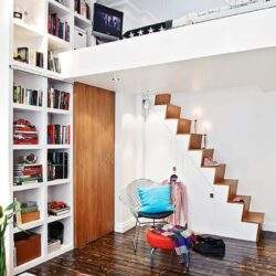 Przestronne mieszkanie z półkami pełnymi książek, nowoczesną schodami i komfortowym miejscem do relaksu, idealne dla poszukujących funkcjonalnej i stylowej aranżacji wnętrz.