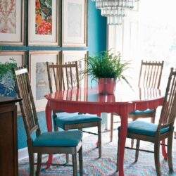 Kolorowy jadalniany stół z czterema krzesłami w stylu vintage, udekorowany zielonym bonsai w czerwonym naczyniu, w nowoczesnym wnętrzu z błękitną ścianą, z nadrukowanymi obrazami na ścianie i eleganckim żyrandolem.