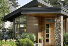 Nowoczesny dom z drewna z dużymi oknami i kamiennym detalem, zielony ogród wokół, elegancka elewacja, przytulny i funkcjonalny, idealny na stylowe mieszkanie, architektura domowa, naturalne materiały.