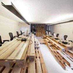 Nowa przestrzeń biurowa z biurkami z palet drewnianych, ergonomiczne krzesła i stanowiska do pracy, industrialny styl, idealne do kreatywnych i innowacyjnych zespołów, skonfigurowane do współpracy i komfortu.