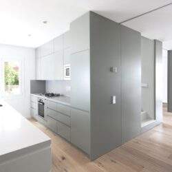 Nowe, jasne i nowoczesne wnętrze kuchni z dużym oknem, minimalistyczny design, białe meble i drewniana podłoga, idealne do optymalizacji przestrzeni i funkcjonalności.