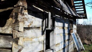 Stara, drewniana chata z wiszącym balkonem i odpadkami wokół, na tle nieba i drzew, w wiejskim otoczeniu, zdjęcie budynku wiejskiego, pokazujące zabytkową architekturę i zaniedbanie, optymalizacja dla słów kluczowych optima.