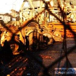 Zepsute maszyny przemysłowe na złomowisku, widok przez drut kolczasty, fabryka i wysłużony sprzęt, przemysłowe otoczenie, degradacja i recykling metali, industrialny klimat, tanie złomy, złomowania sprzętu przemysłowego.