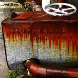 Zbiornik na olej opałowy z napisaniem "Zalewanie furolu" na zardzewiałej powierzchni, elementy instalacji oraz rury, scenka zewnętrzna, przemysłowa, w roli głównej urządzenia grzewcze, odpady, metale.