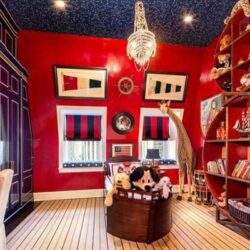 Rozświetlony pokój dziecięcy z czerwonymi ścianami i dużą literą giraffa, otoczony półkami z książkami i zabawkami, idealny do rozwoju i nauki dla dzieci.