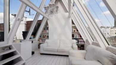 Przestronny salon z dużymi oknami na strychu, nowoczesny design, białe meble, biblioteka i elegancki żyrandol, idealny do relaksu i czytania.