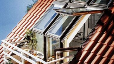 Nowoczesne okna dachowe na strychu, balkon z poręczą w domu z czerwonym dachem, widok pod słońce, komfort i estetyka dachowych rozwiązań okiennych.