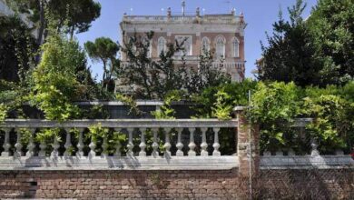 Trójwymiarowa fotografia klasycznej willi z ozdobnym balkonem i ozdobnym ogrodzeniem w stylu art déco, otoczonej zielonymi drzewami w słoneczny dzień.