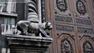 Precyzyjna brama wejściowa z rzeźbionymi elementami i wagą, wykończona detalami z ciemnego drewna, na tle zabytkowej architektury, symbol klasy i elegancji, idealna dla projektów architektonicznych.