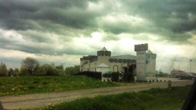 Przydrożny hotel i restauracja z parkingiem, otoczona zielenią, pod ciemnym, burzowym niebem, w okolicy miasta, idealna na relaks i odpoczynek.