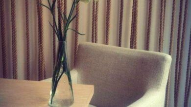 Rzeźbione kwiaty w wazonie na drewnianym stole z jasnym fotelem w tle, elegancka aranżacja wnętrza biura lub salonu, stylowe wyposażenie, inspirujące miejsce do pracy czy spotkań, aranżacja biura zgodna z trendami designu.