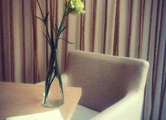Rzeźbione kwiaty w wazonie na drewnianym stole z jasnym fotelem w tle, elegancka aranżacja wnętrza biura lub salonu, stylowe wyposażenie, inspirujące miejsce do pracy czy spotkań, aranżacja biura zgodna z trendami designu.