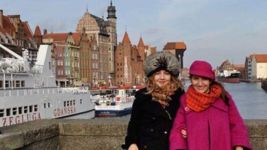 PaniDyrektor.pl, ożywiona kobieta na tle starówki Gdańska, ulica nad Motławą, w ciepłej zimowej odzieży, turystyka i podróże, urokliwa atmosfera miasta, polskie miasto, turystyka w Polsce, piękne miejsca.